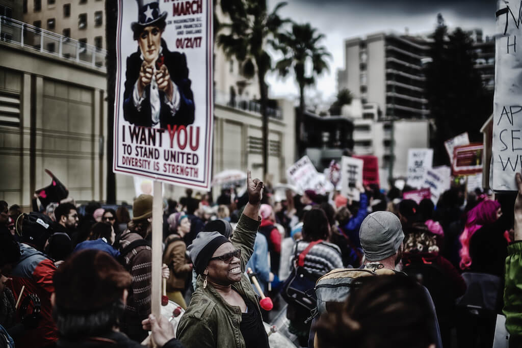 Image Description: An image from a protest featuring a sign with Uncle Sam which reads “I Want You To Stand United: Diversity is Strength”